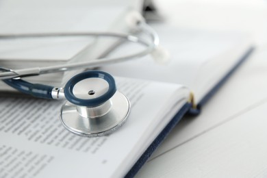 Photo of One new medical stethoscope and books on white wooden table, closeup