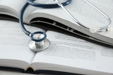 Photo of One medical stethoscope and books on white table, closeup