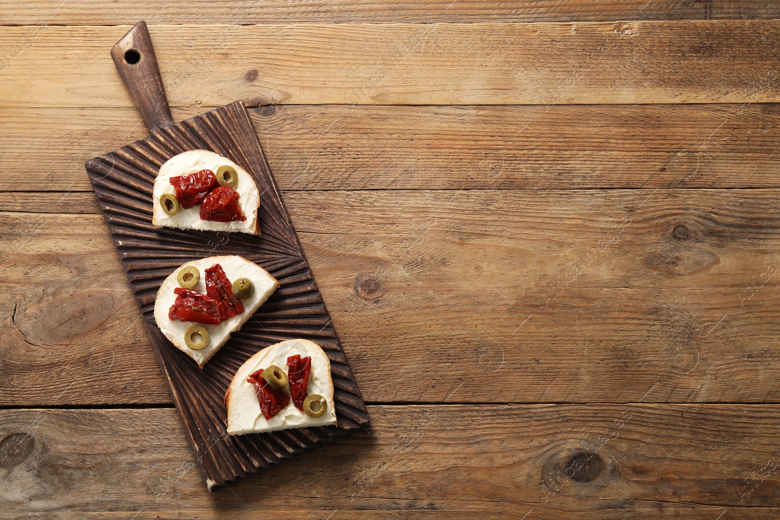 Photo of Delicious bruschettas with ricotta cheese, sun dried tomatoes and olives on wooden table, top view. Space for text