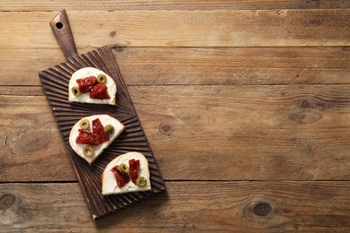 Delicious bruschettas with ricotta cheese, sun dried tomatoes and olives on wooden table, top view. Space for text