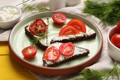 Delicious bruschettas with ricotta cheese, dill, fresh and sun dried tomatoes on yellow wooden table, closeup