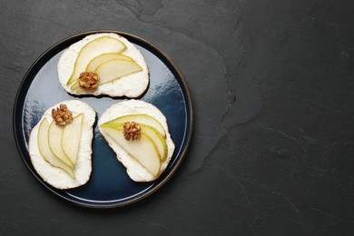 Delicious bruschettas with ricotta cheese, pears and walnuts on dark textured table, top view. Space for text