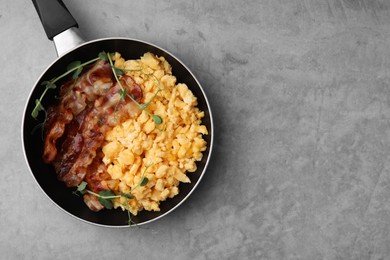 Photo of Delicious scrambled eggs with bacon in frying pan on grey table, top view. Space for text