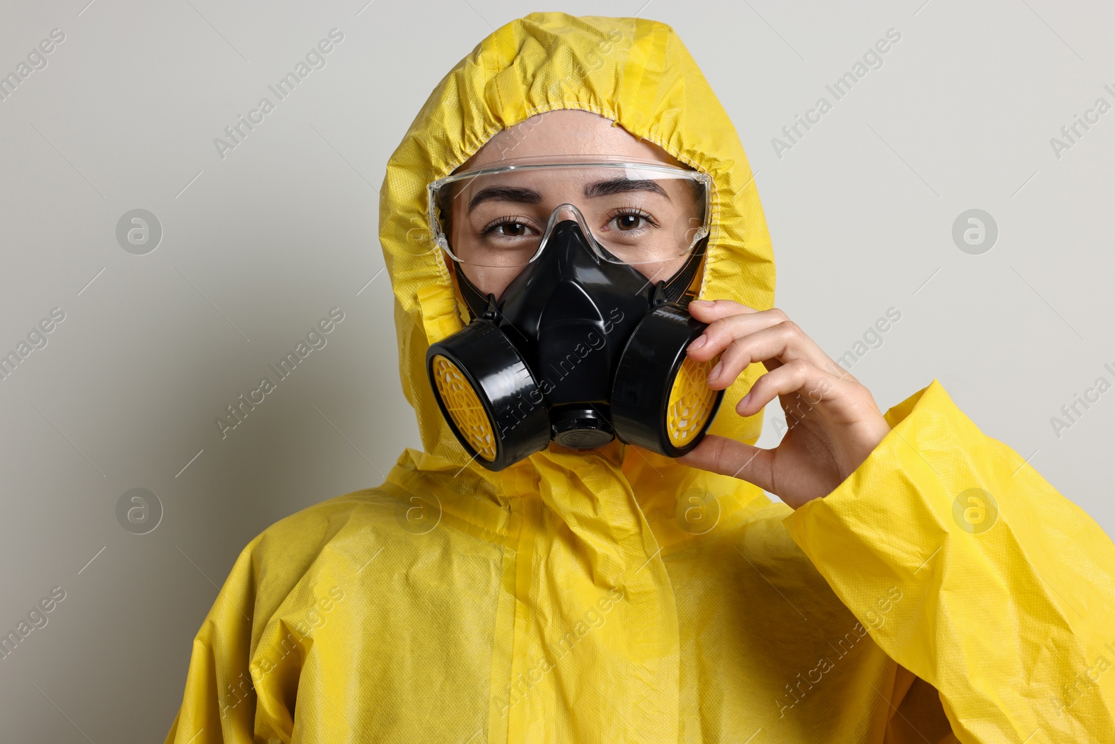 Photo of Worker in respirator, protective suit and glasses on grey background