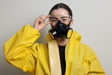 Photo of Worker in respirator, protective suit and glasses on grey background