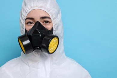 Worker in respirator and protective suit on light blue background, space for text