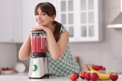 Young woman making delicious smoothie with blender at white marble table in kitchen