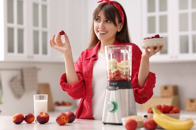 Young woman making delicious smoothie with blender at white marble table in kitchen