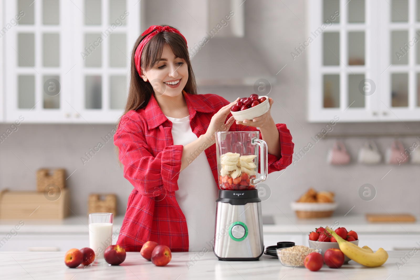 Photo of Young woman making delicious smoothie with blender at white marble table in kitchen