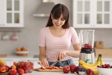 Photo of Young woman making delicious smoothie with blender at white marble table in kitchen