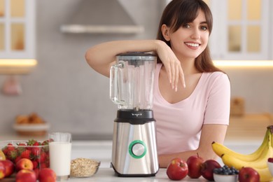 Young woman making delicious smoothie with blender at white marble table in kitchen