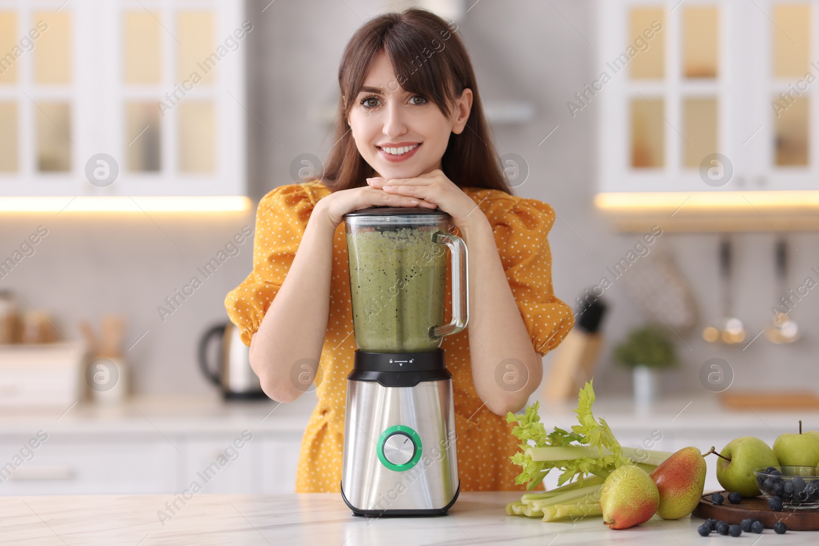 Photo of Young woman making delicious smoothie with blender at white marble table in kitchen