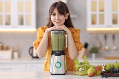 Photo of Young woman making delicious smoothie with blender at white marble table in kitchen