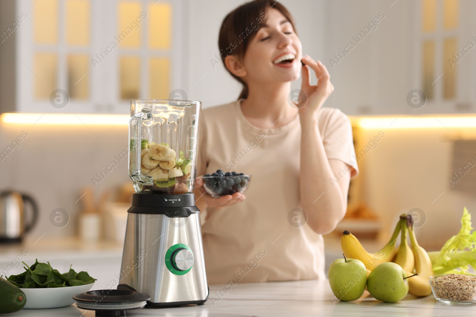 Photo of Young woman making delicious smoothie with blender at white marble table in kitchen