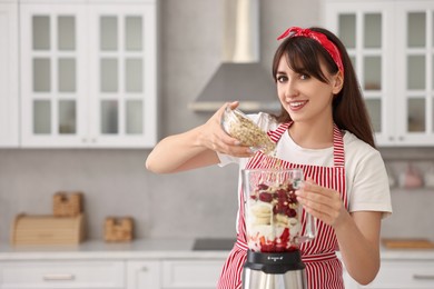 Photo of Young woman making delicious smoothie with blender in kitchen