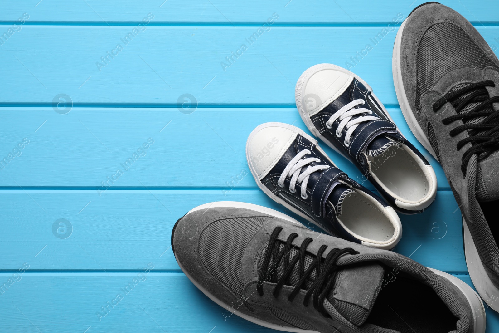 Photo of Big and small shoes on light blue wooden table, top view. Space for text