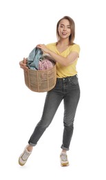 Happy young housewife with basket full of laundry on white background