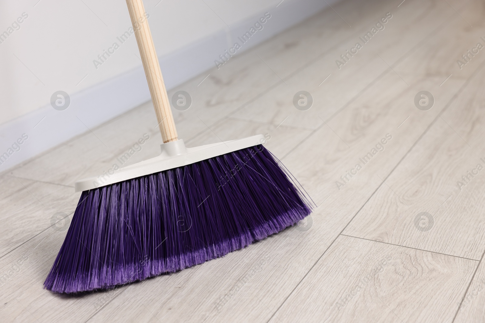 Photo of Sweeping wooden floor with bright broom indoors, space for text