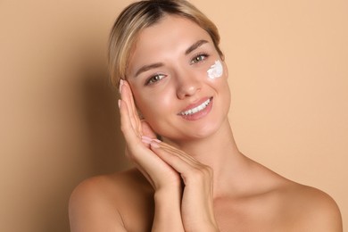 Beautiful woman with cream on her face against beige background