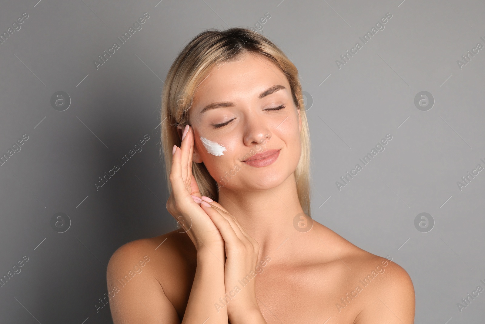 Photo of Beautiful woman with cream on her face against grey background