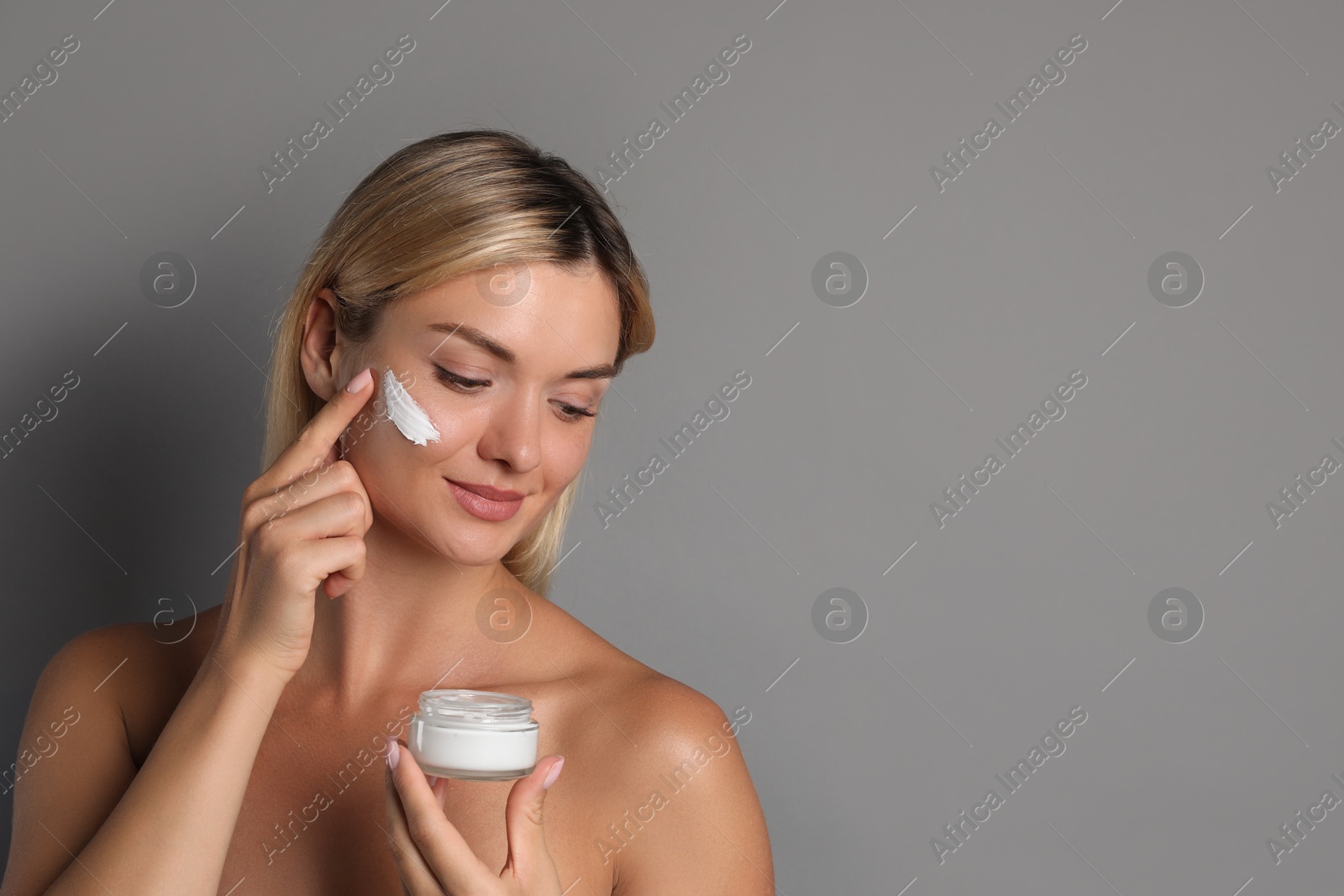 Photo of Beautiful woman applying face cream on grey background, space for text