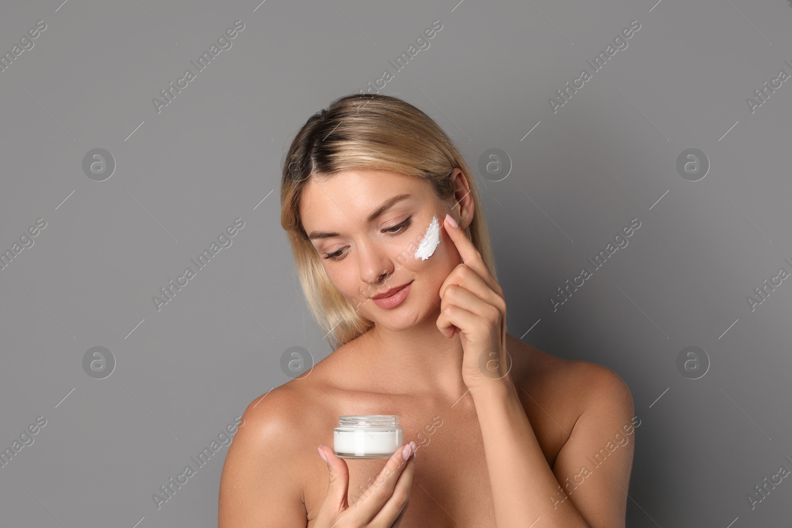 Photo of Beautiful woman applying face cream on grey background