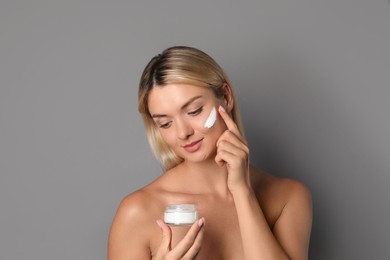 Beautiful woman applying face cream on grey background