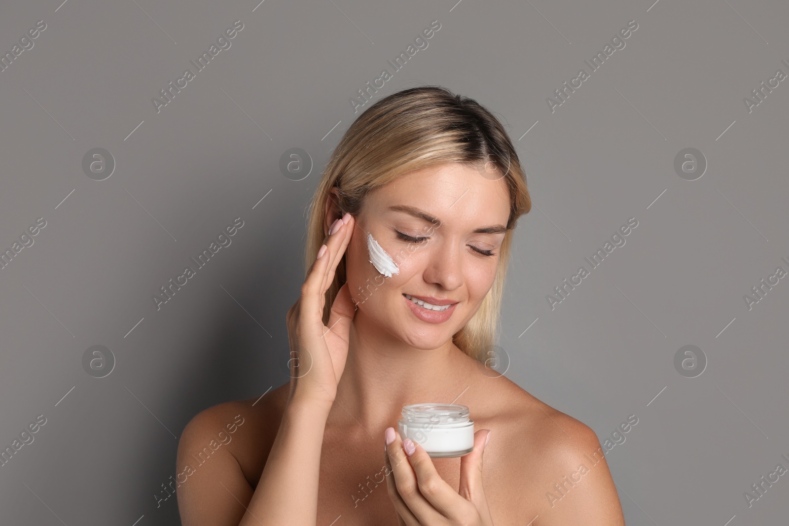 Photo of Beautiful woman with cream on her face against grey background