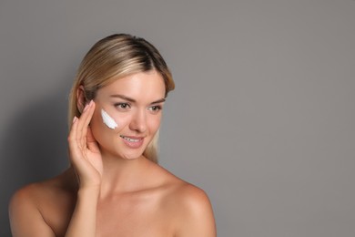 Photo of Beautiful woman with cream on her face against grey background, space for text