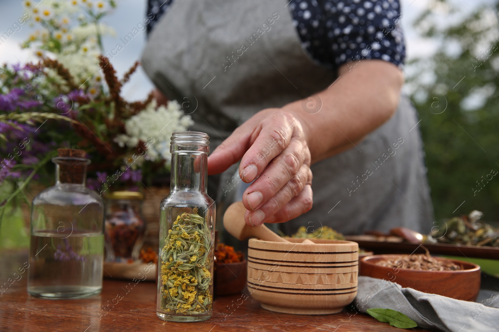 Photo of Senior woman making tincture at table outdoors, closeup