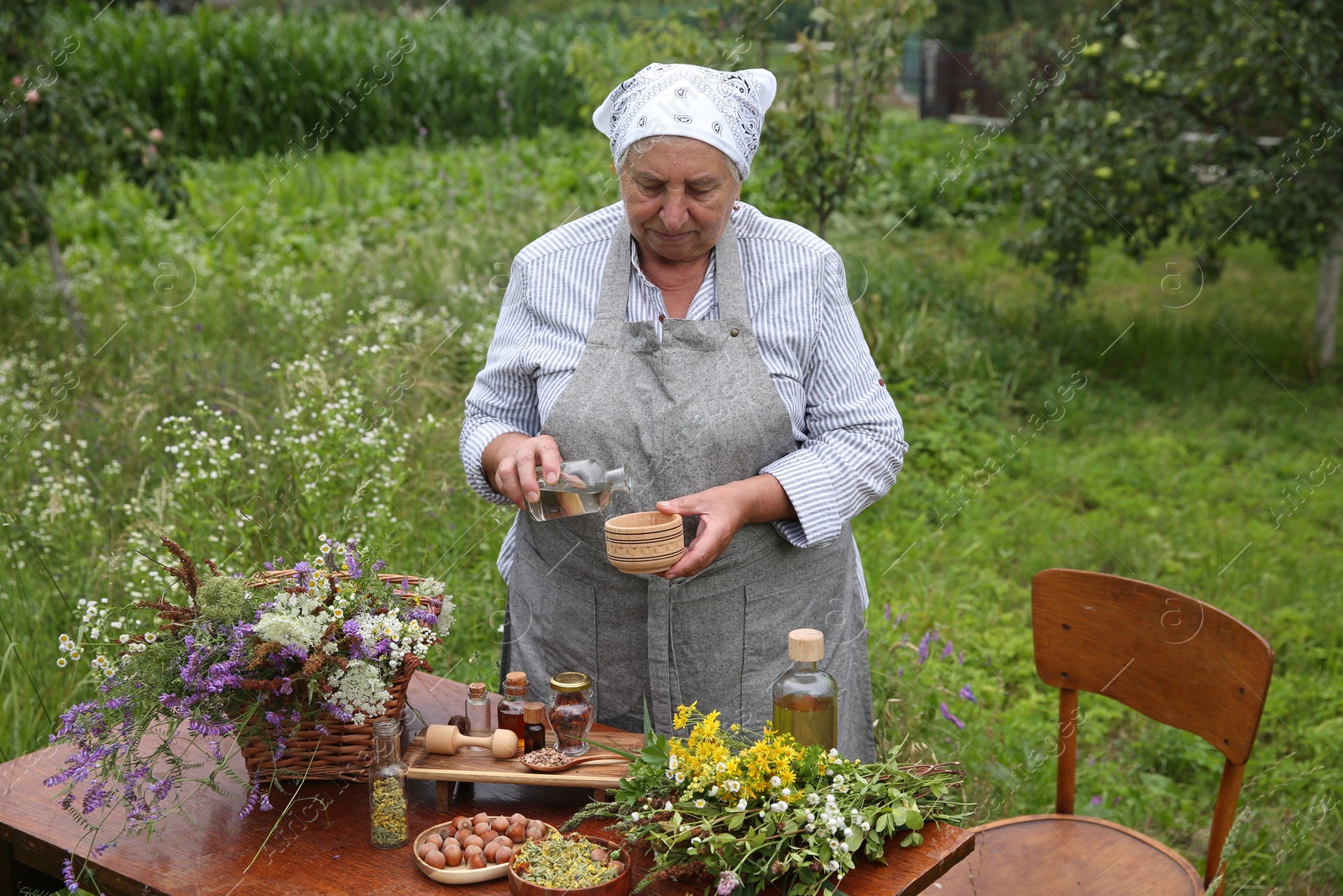 Photo of Senior woman making tincture at table outdoors