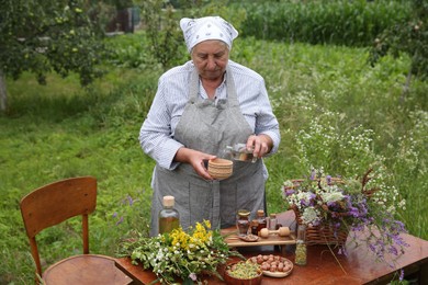 Photo of Senior woman making tincture at table outdoors