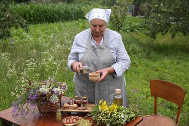 Photo of Senior woman making tincture at table outdoors