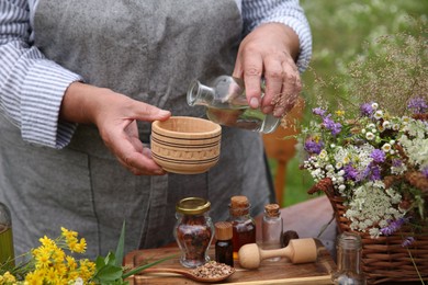 Photo of Senior woman making tincture at table outdoors, closeup