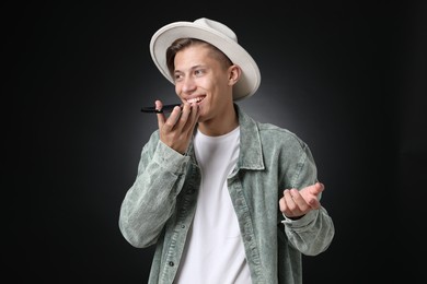 Photo of Young man recording voice message via smartphone on dark background