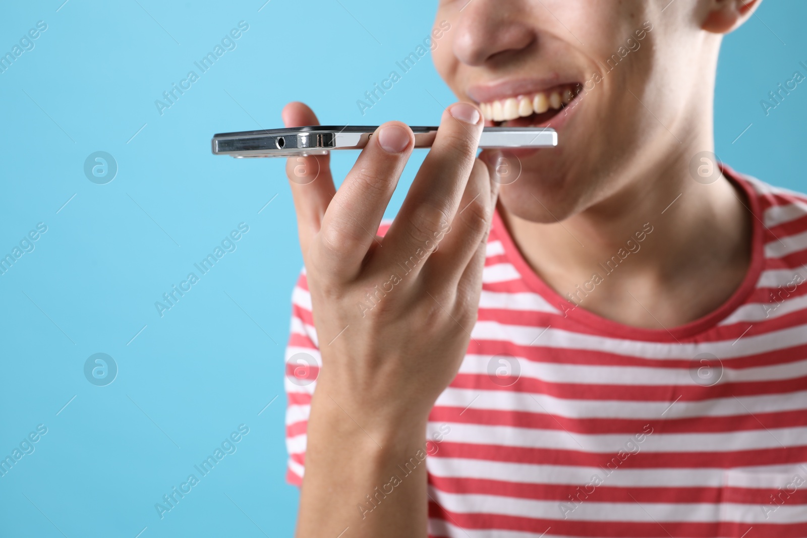 Photo of Young man recording voice message via smartphone on light blue background, closeup. Space for text