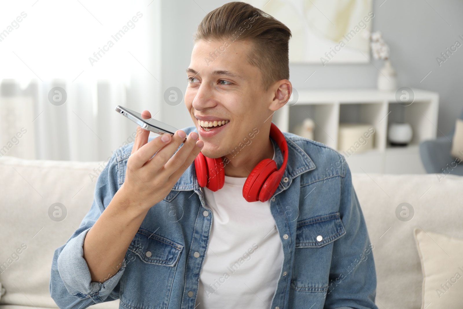 Photo of Young man recording voice message via smartphone at home