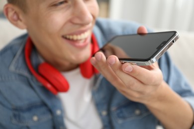 Photo of Young man recording voice message via smartphone at home, selective focus