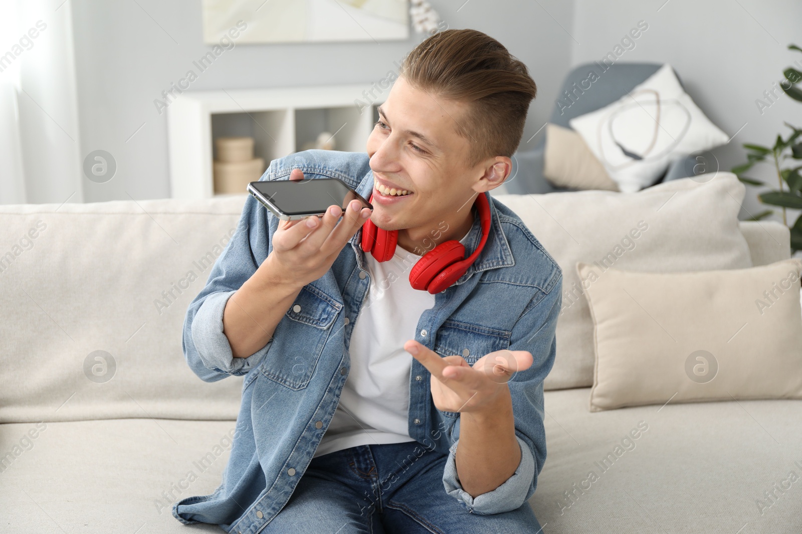 Photo of Young man recording voice message via smartphone at home