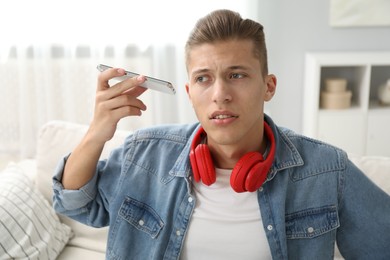 Photo of Young man with smartphone listening to voice message at home