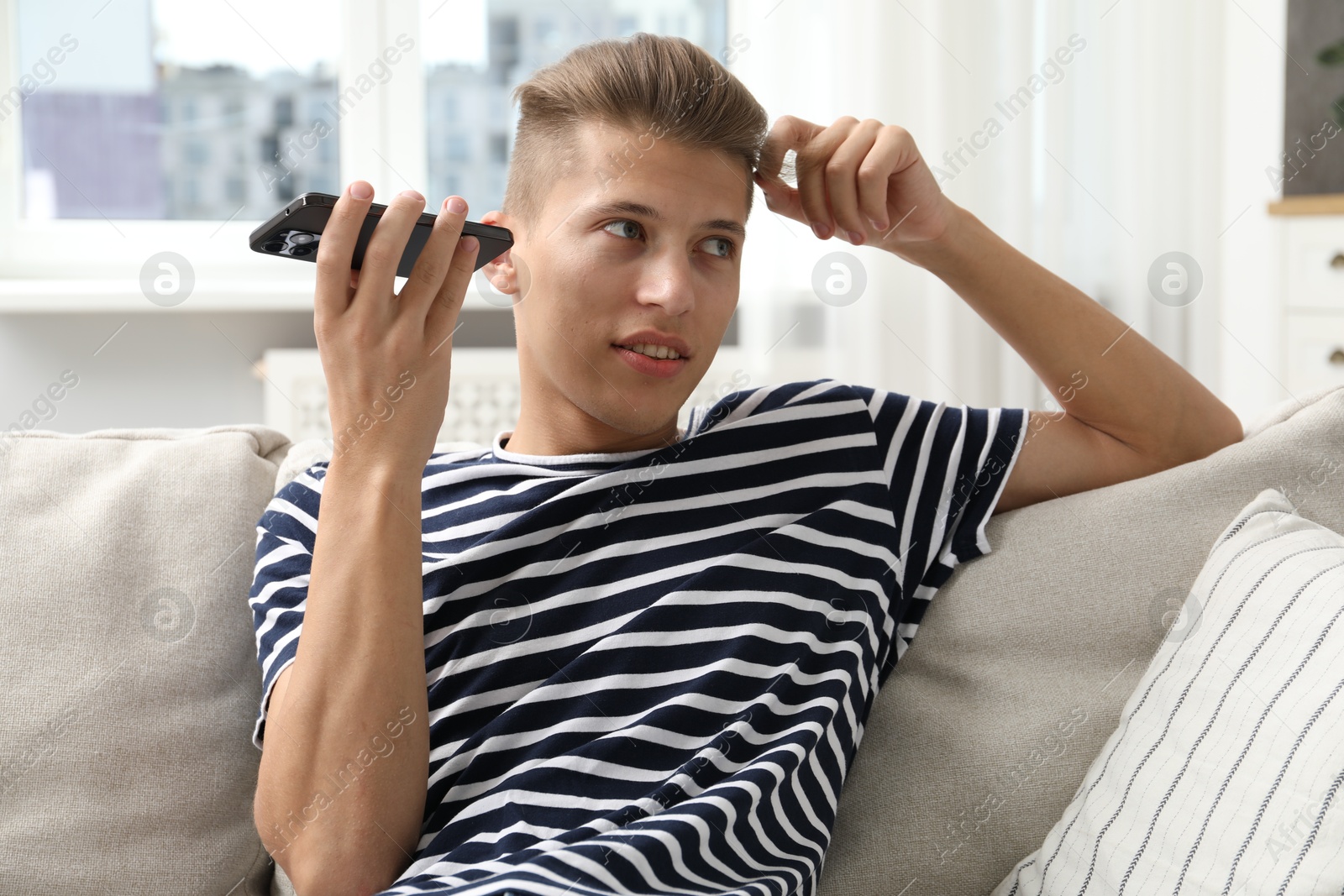 Photo of Young man with smartphone listening to voice message at home