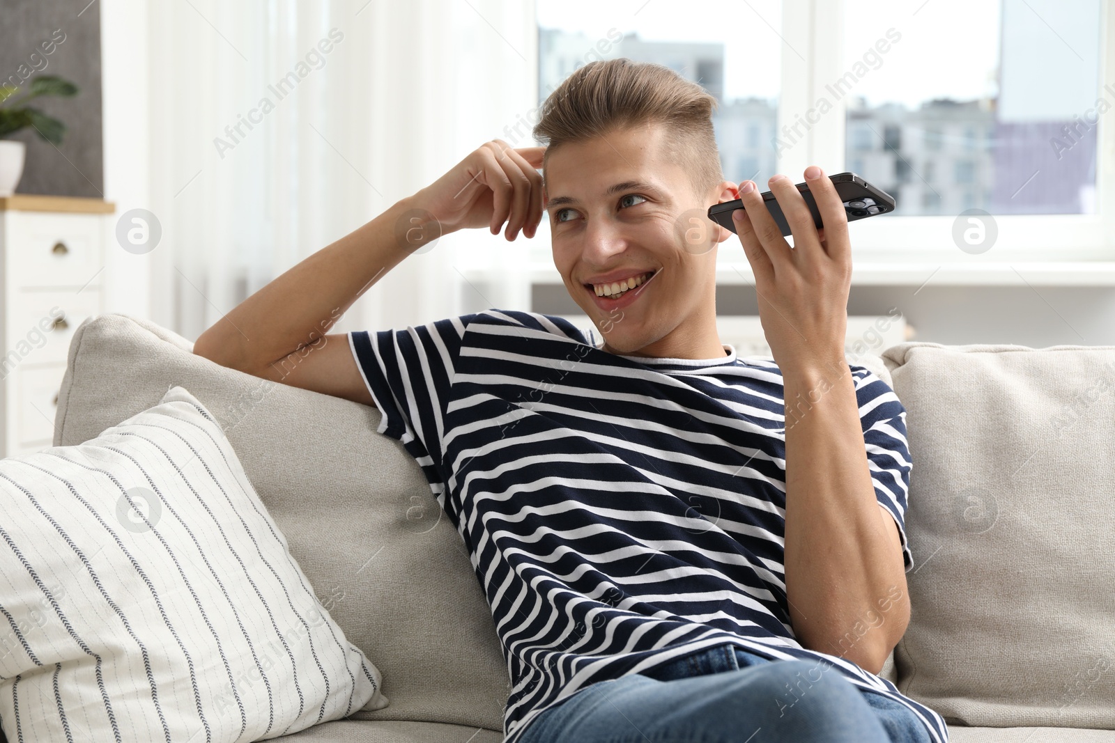 Photo of Young man with smartphone listening to voice message at home