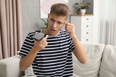 Photo of Young man recording voice message via smartphone at home