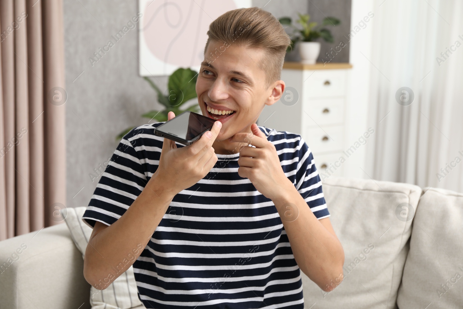 Photo of Young man recording voice message via smartphone at home