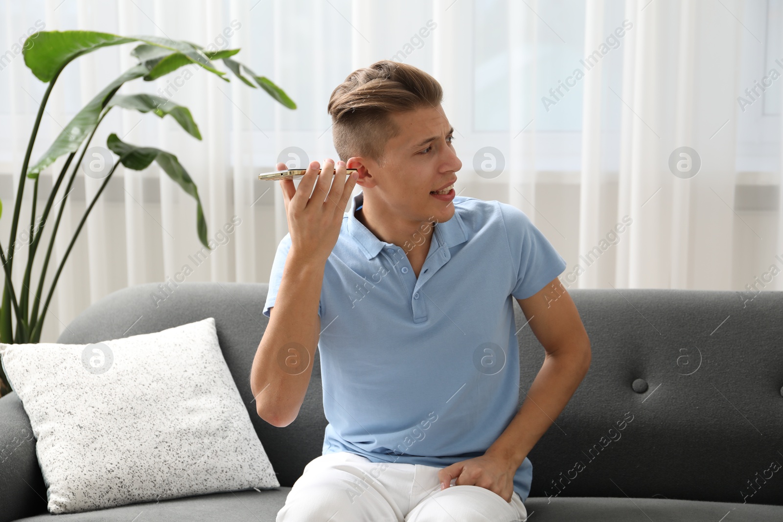 Photo of Young man with smartphone listening to voice message at home