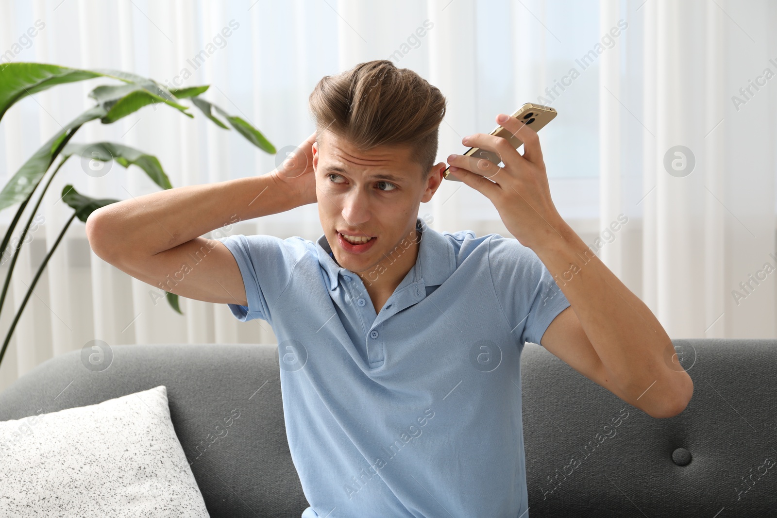 Photo of Young man with smartphone listening to voice message at home