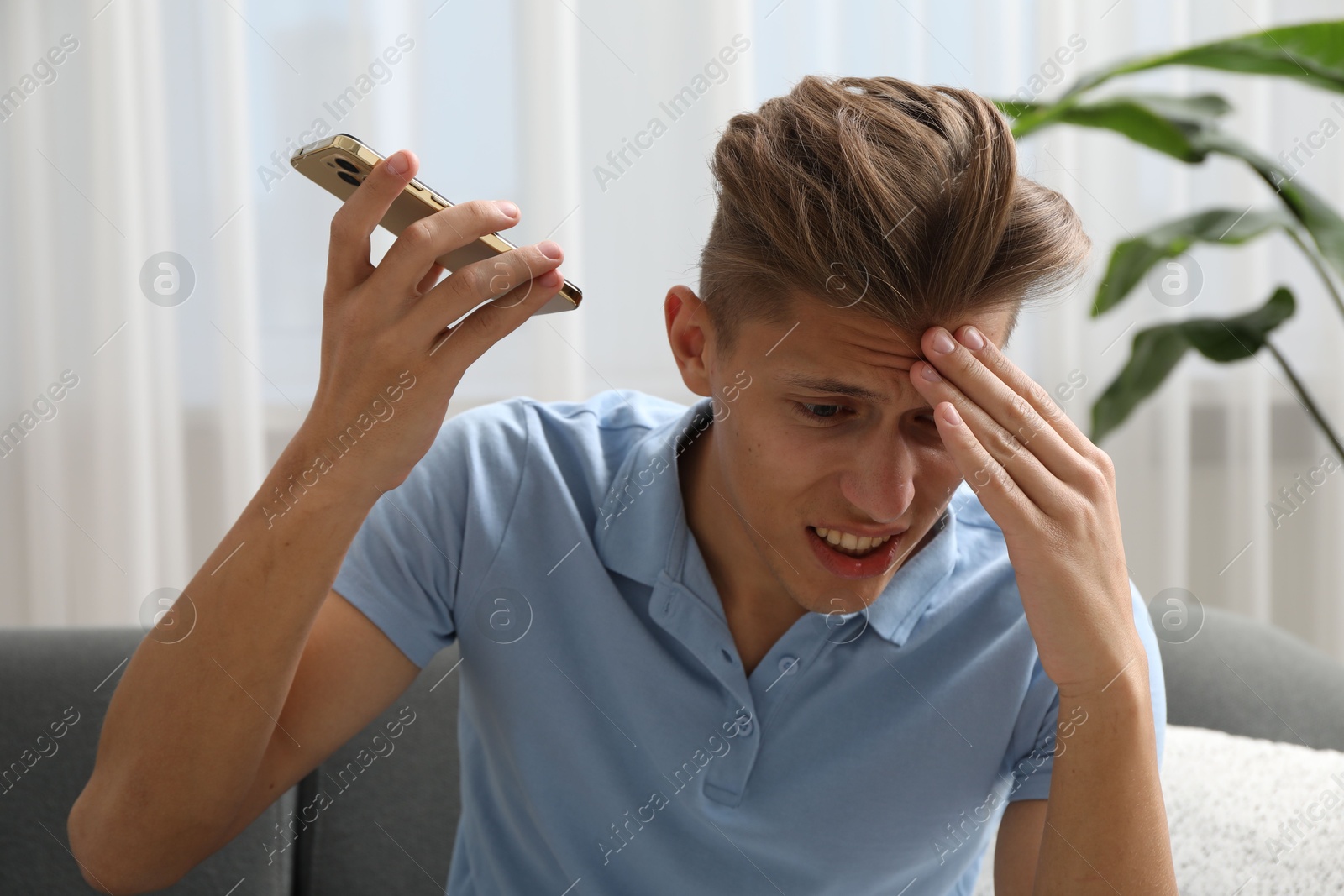 Photo of Young man with smartphone listening to voice message at home