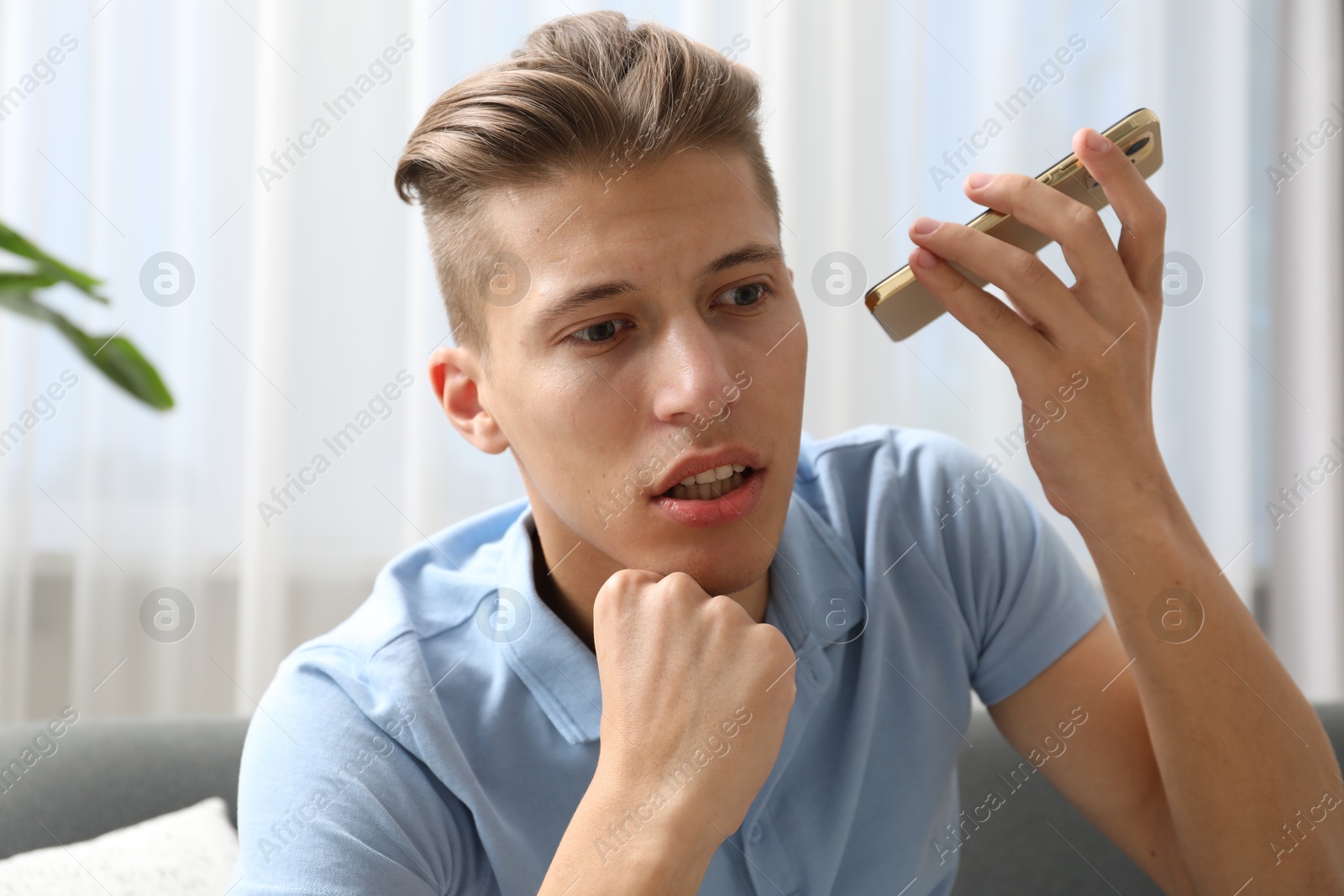 Photo of Young man with smartphone listening to voice message at home