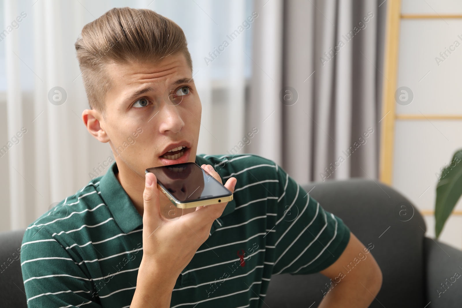 Photo of Young man recording voice message via smartphone at home