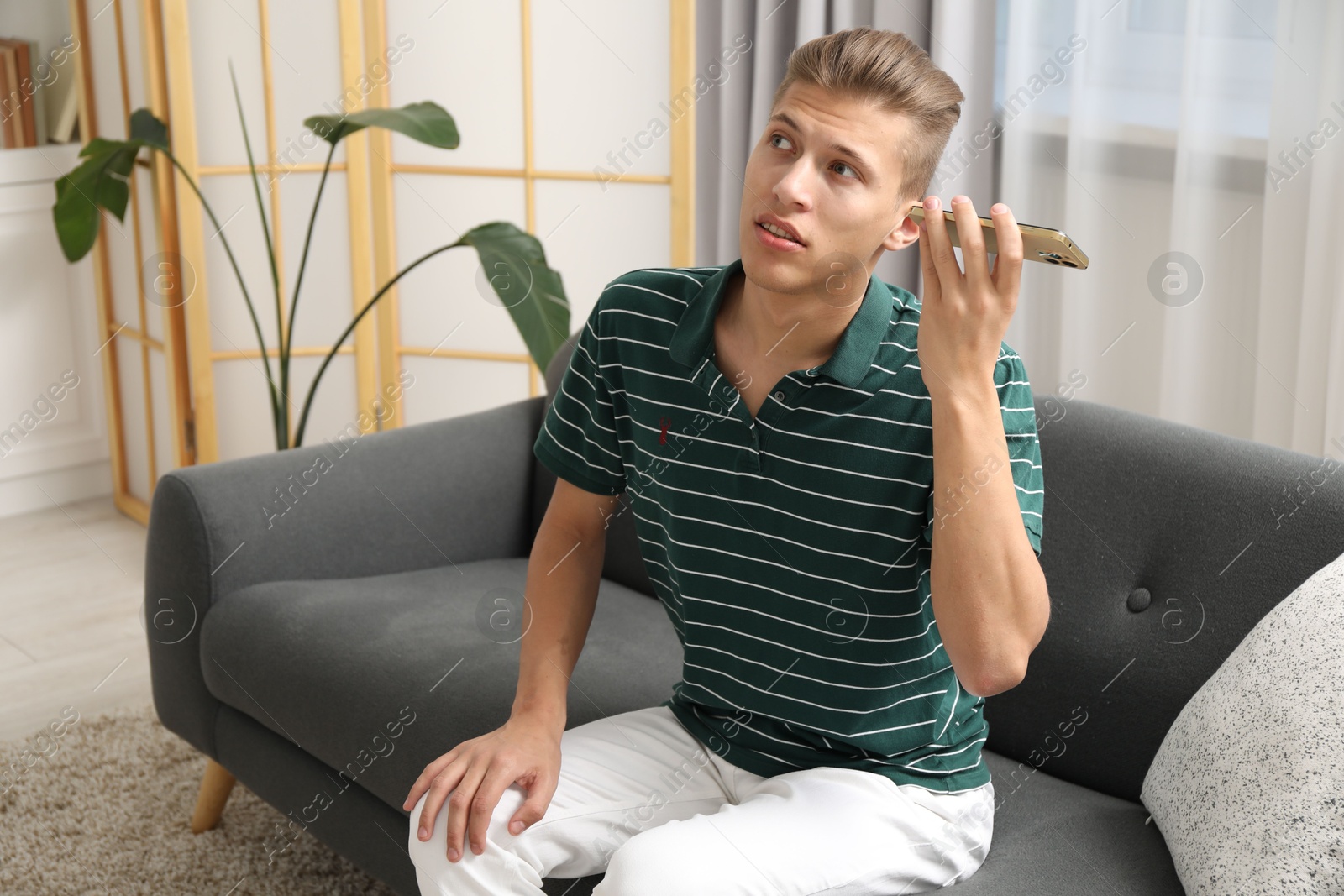 Photo of Young man with smartphone listening to voice message at home